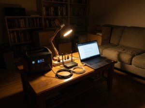 A realistic small apartment interior during a power outage, focused on a working backup power setup.

Scene:
A modest apartment living space at night. Main ceiling lights are OFF.

Active setup elements:
– a portable power station actively running with screen ON
– connected devices:
– Wi-Fi router with indicator lights ON
– laptop turned ON
– small desk lamp providing focused light

Setup clarity:
– cables visible and neatly connected
– power strip used only for essential devices
– compact, space-efficient arrangement

Apartment cues:
– limited space
– simple furniture
– realistic lived-in look

Mood:
functional, practical, reassuring

Style:
editorial technical photography
realistic, non-commercial

Strict rules:
– no people
– no brand logos
– no text overlays
– no generators
– no solar panels
– no outdoor scenes

Ultra-high resolution, suitable for a backup power setup guide category for apartments.